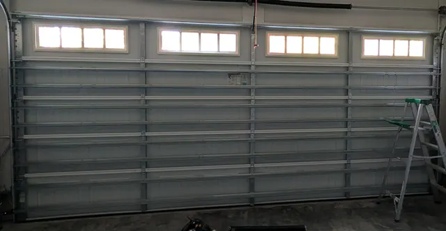 Inside view of a garage door with a row of window panels and a torsion spring system above it